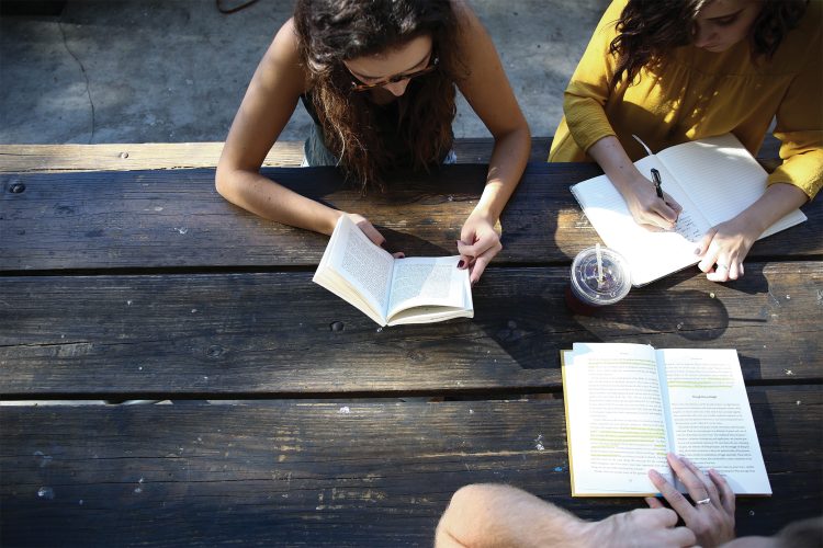 People sitting around picnic table with books