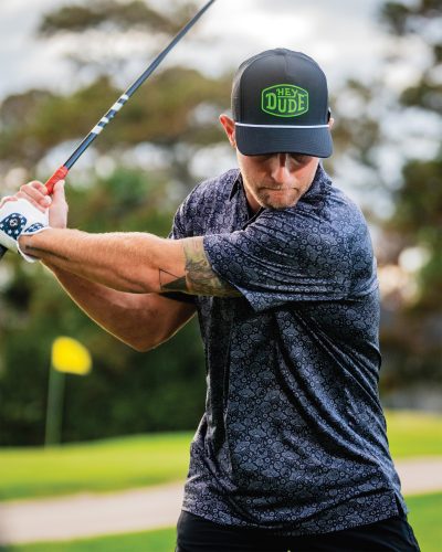 A man golfs while wearing items from the Pins & Aces X Hey Dude collaboration.
