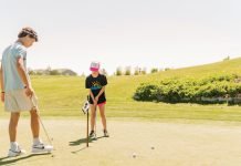Two kids putt into a golf hole.