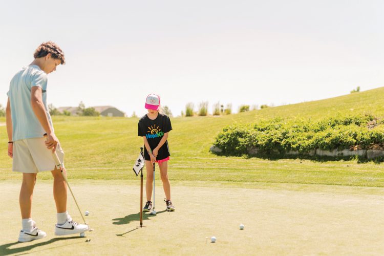 Two kids putt into a golf hole.