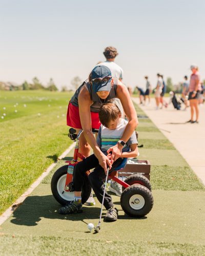 A women assists a child putting on the golf course.