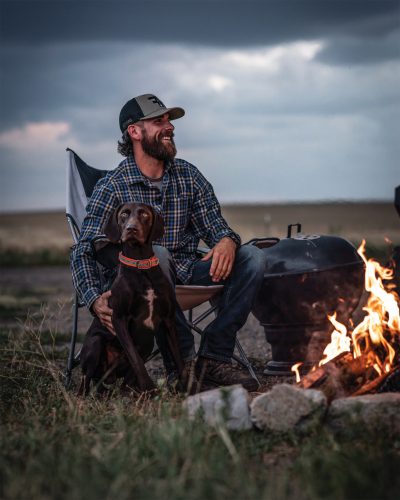 Anthony Ferro relaxes by a fire with a hunting dog