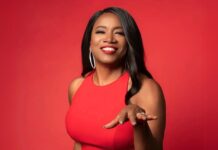 Portrait of singer Eugenie Jones against a bold red background, wearing a sleeveless red dress and smiling confidently toward the camera. She gestures with one hand extended, conveying warmth and charisma, with studio lighting highlighting her expressive stage presence.