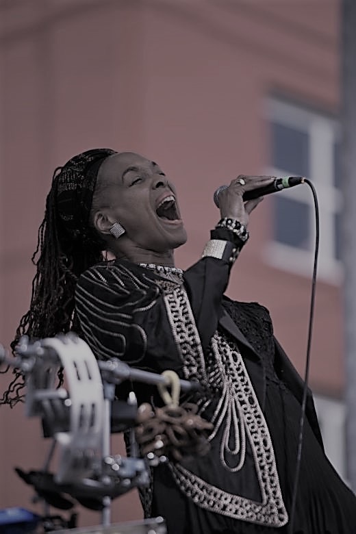 Black-and-white photo of singer Linda Theus-Lee performing onstage, holding a microphone mid-song.