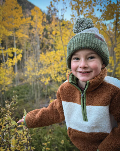 Child posing in Keep the Littles Wild outdoor gear in front of Aspen trees.