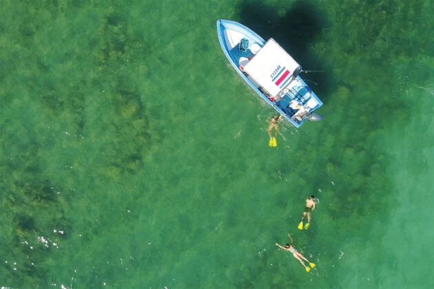 People swim in the ocean around a boat at Casa Chameleon.