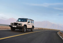 A First Look at the INEOS Grenadier Retro Inspired 4×4 The INEOS Grenadier drives on a road in front of mountains.