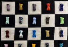 Grid-style artwork composed of multiple small, colorful glass torso-shaped forms arranged in neat rows on individual square panels. Each piece varies in color and texture, set against contrasting light and dark backgrounds, creating a quilt-like composition that emphasizes repetition, variation, and individuality within the series.