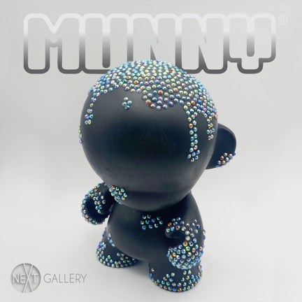 Promotional image of a customized KidRobot MUNNY figure standing against a light gray background. The black vinyl character is covered in small, colorful bead-like embellishments across its head and body, creating a textured, sculptural surface. The word “MUNNY” appears above the figure in bold lettering, emphasizing the designer toy theme.