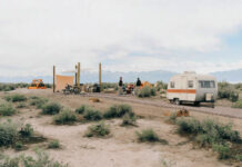 People relax around a campfire with an RV at Ramble Camp.