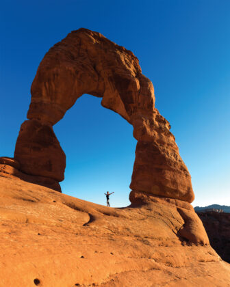 Person poses in front of Delicate Arch in Arches National Park, Moab.