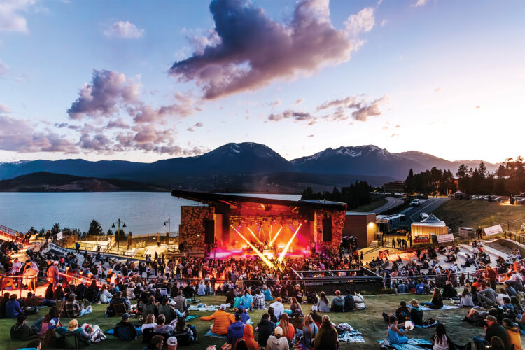 A concert takes place at Mountain Music Mondays at Dillon Amphitheater with views of the mountains and reservoir.