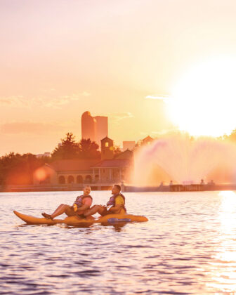 People kayak on a lake in front of the city skyline.