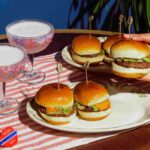 Image showing four slider style burgers as well as two pink cocktails on an American Flag themed place setting.