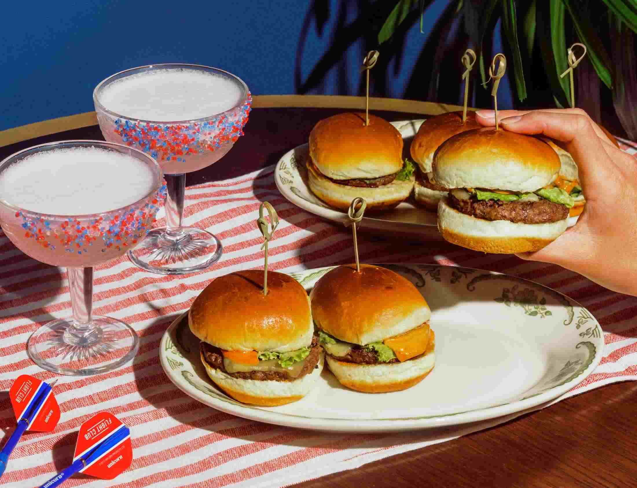 Image showing four slider style burgers as well as two pink cocktails on an American Flag themed place setting.