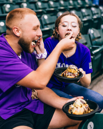 Couple feeds each other the Dubai Cinnamon Roll at Coors Field.