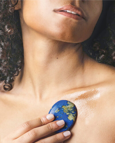 Woman poses while rubbing skincare on her chest.