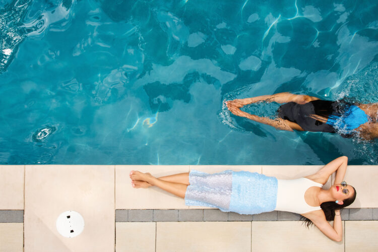 Woman swims in pool while another lounges on the side.