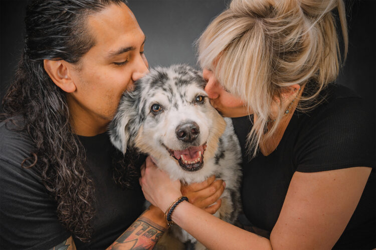 Two people kiss their dog in a photo by Fetch Photo Truck.