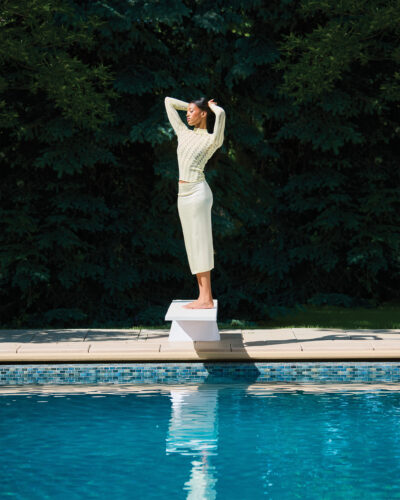 Woman poses on diving board over pool.