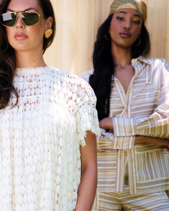 Two woman pose in a backyard in front of bamboo fence.