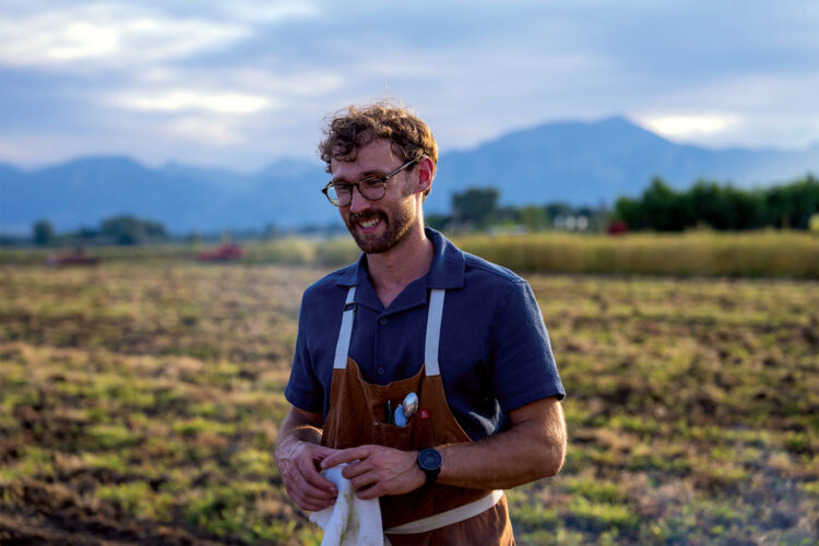 Man poses in a field in an apron at Freehand Provisions.