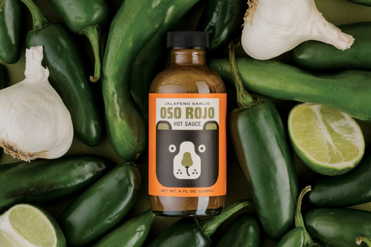 Bottle of Oso Rojo Hot Sauce surrounded by peppers.