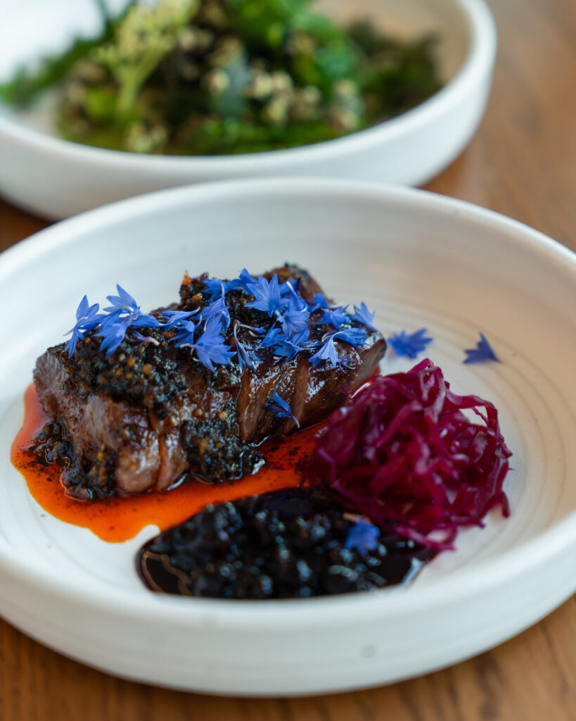 Steak garnished with purple flowers and beet strings at chef Kelly Whitaker's SHEEP.