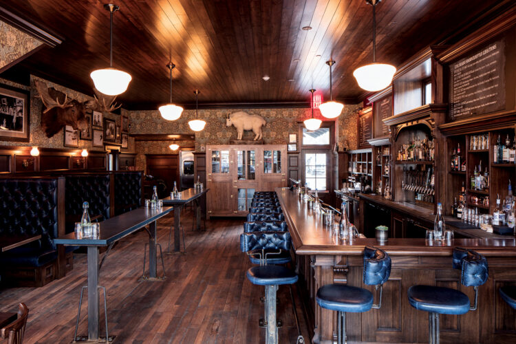 Warm wood-paneled pub interior with leather booths, bar seating, pendant lights, and mounted wildlife decor.
