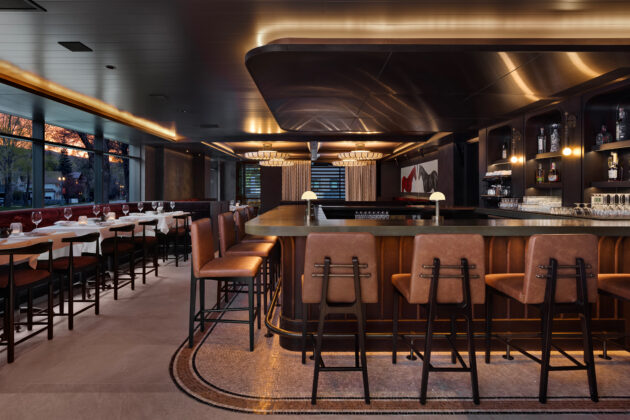 Elegant restaurant interior with a curved bar, leather stools, warm lighting, and white-tablecloth dining.