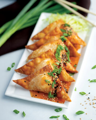 Crispy fried wontons topped with sesame seeds, green onions, and a savory orange sauce.