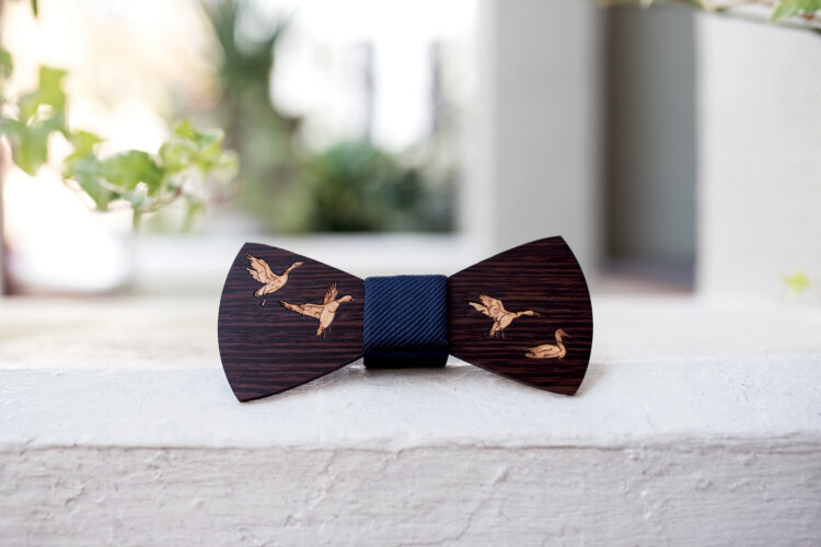Wooden bow tie engraved with flying ducks and finished with a navy fabric center.