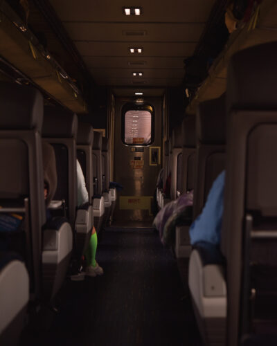 Interior view down the aisle of an Amtrak passenger train, with rows of seats and travelers aboard.