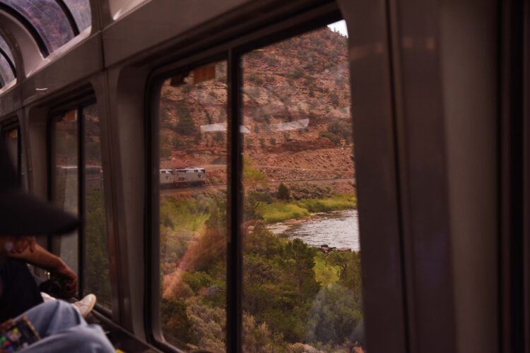View from an Amtrak train window of another train traveling alongside a river through a rocky canyon.