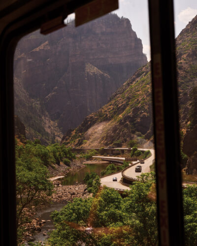 Winding highway, river and towering canyon walls seen through the window of an Amtrak train.