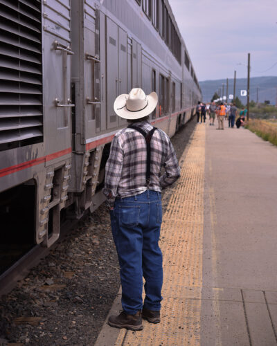 Person in a cowboy hat standing beside an Amtrak train at a station platform in Colorado.