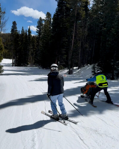 Woman follows behind adaptive skier with Ignite Adaptive Sports.
