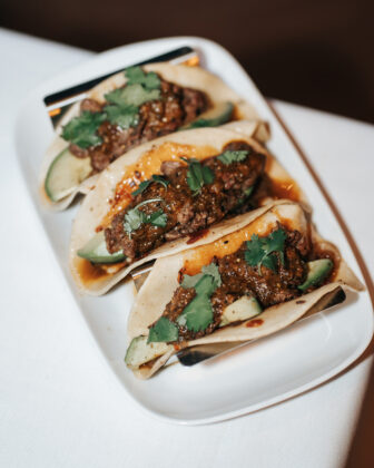 Three beef tacos topped with cilantro and avocado on a white serving platter.