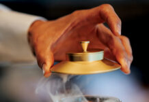 Smoked amber cocktail revealed beneath a gold-topped cloche in a cut-crystal glass.