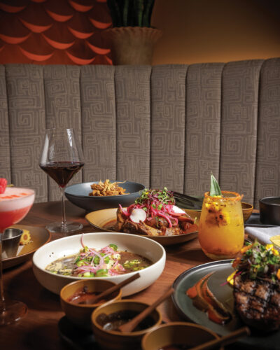 Table spread at El Tule featuring colorful Mexican dishes, cocktails and a glass of red wine.