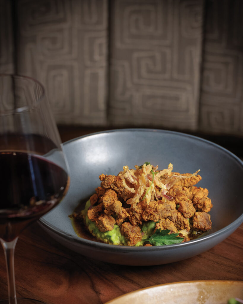 Crispy fried bites served over avocado with fried onions and a glass of red wine.
