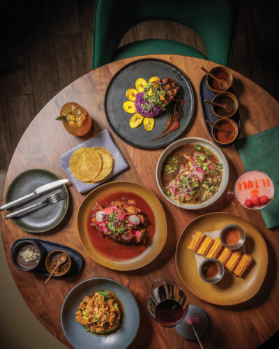 Overhead view of an El Tule dining spread with steak, braised meat, tortillas, churros, cocktails and other dishes.