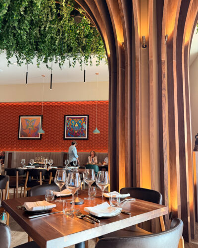 El Tule dining room with warm wood details, greenery, colorful artwork and an orange textured accent wall.