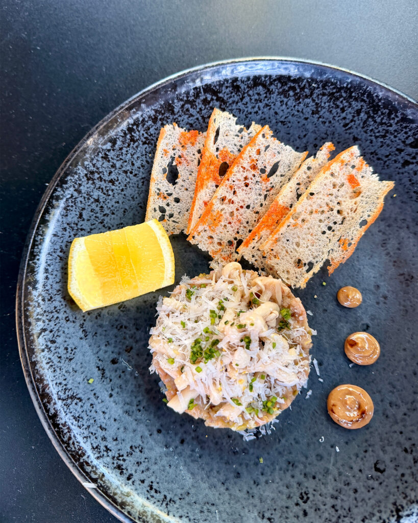 Plated tartare topped with shaved cheese and chives, served with crisp bread, lemon, and sauce.