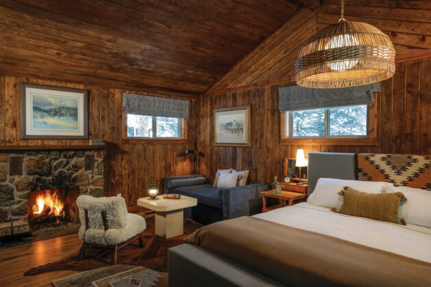 Rustic guest room at Tumbling River Ranch in Colorado with wood-paneled walls, a stone fireplace, cozy seating and a bed with Western-inspired textiles.