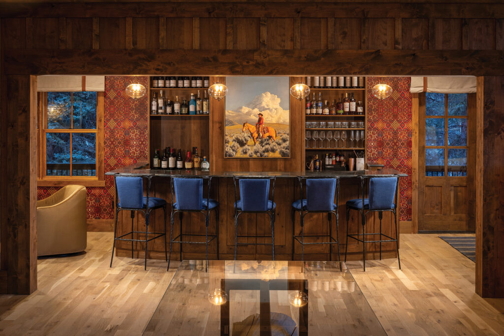 Wood-paneled bar at Tumbling River Ranch with blue barstools, vintage-style pendant lights, patterned wall coverings and Western artwork.