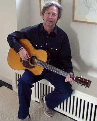 Eric Clapton eated with an acoustic guitar while wearing a black Western shirt from Rockmount Ranch Wear.