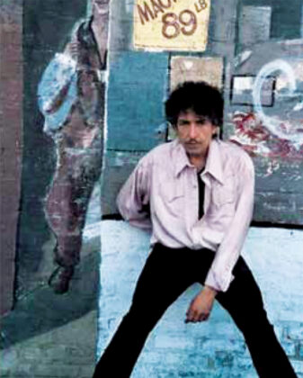 Bob Dylan wearing a Western-style shirt while standing outside a storefront in a vintage photograph.