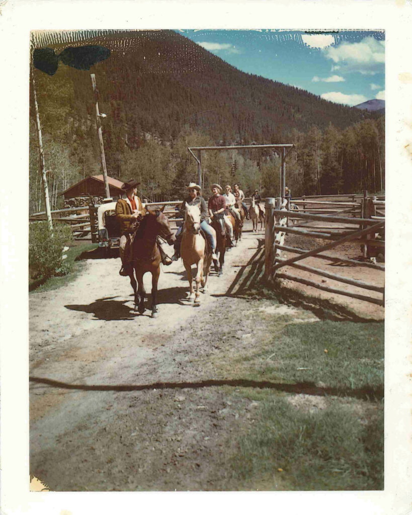 Vintage color photograph of guests on horseback leaving the corrals at Tumbling River Ranch surrounded by Colorado mountain scenery.