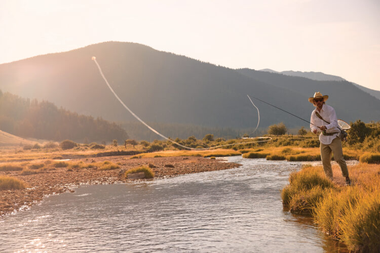 A fly fisherman casts his line across a winding mountain stream in the warm evening light.